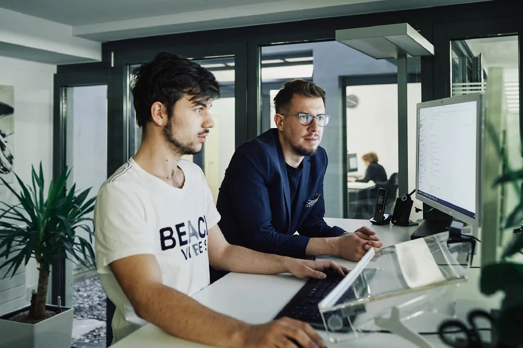 arvenio Mitarbeiter Aaron Sommer und Dominik Wubs vor Bildschirmen