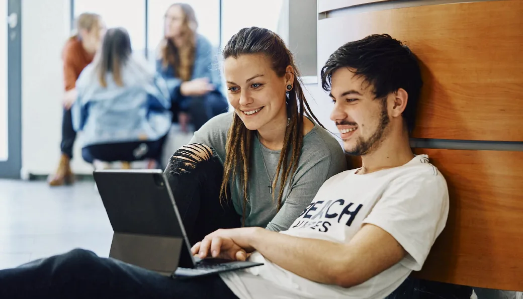 Zwei Mitarbeiter sitzend mit Blick auf einen Laptop