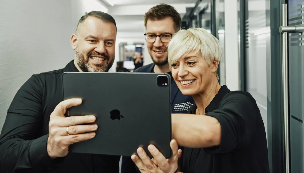 Wir sind Ihr Partner mit SEA-Erfahrung Drei arvenio Mitarbeiter vor einem Tablet-PC