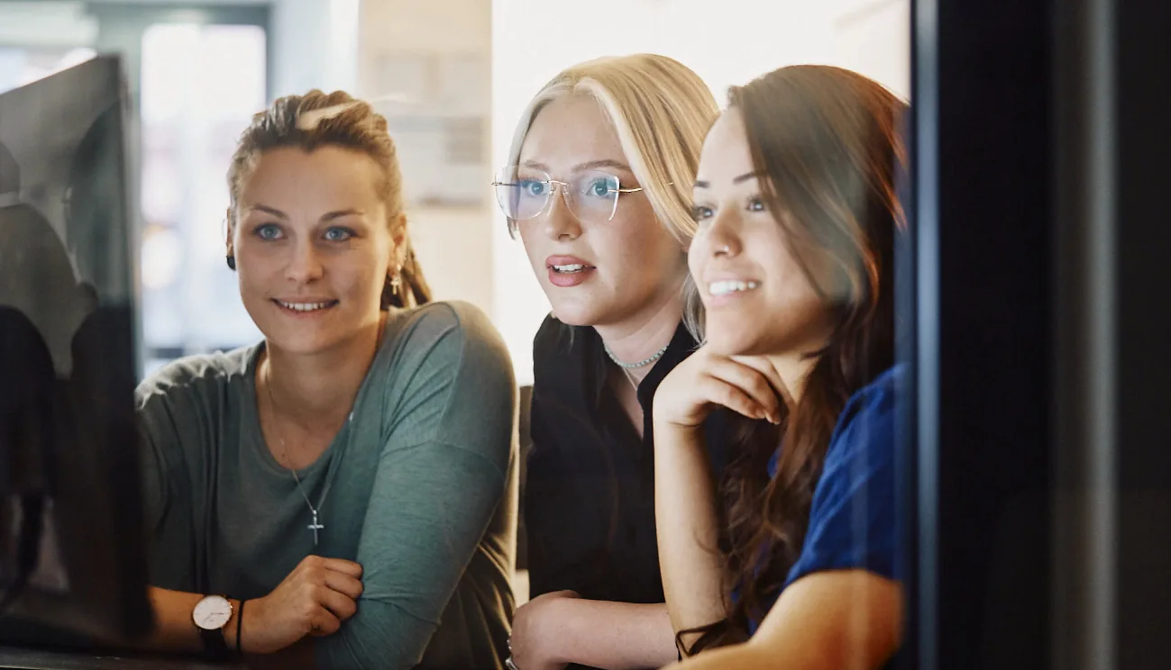 Wir bieten Grafikdesign mit Freude Drei freundliche Mitarbeiterinnen in einem Büro